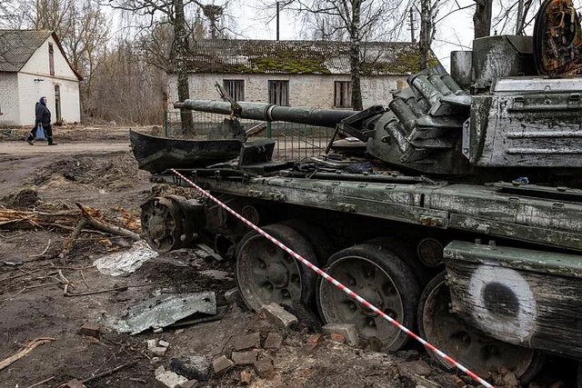 Many Russian military vehicles were destroyed in the war in Ukraine. A Ukrainian woman walks past a wrecked tank